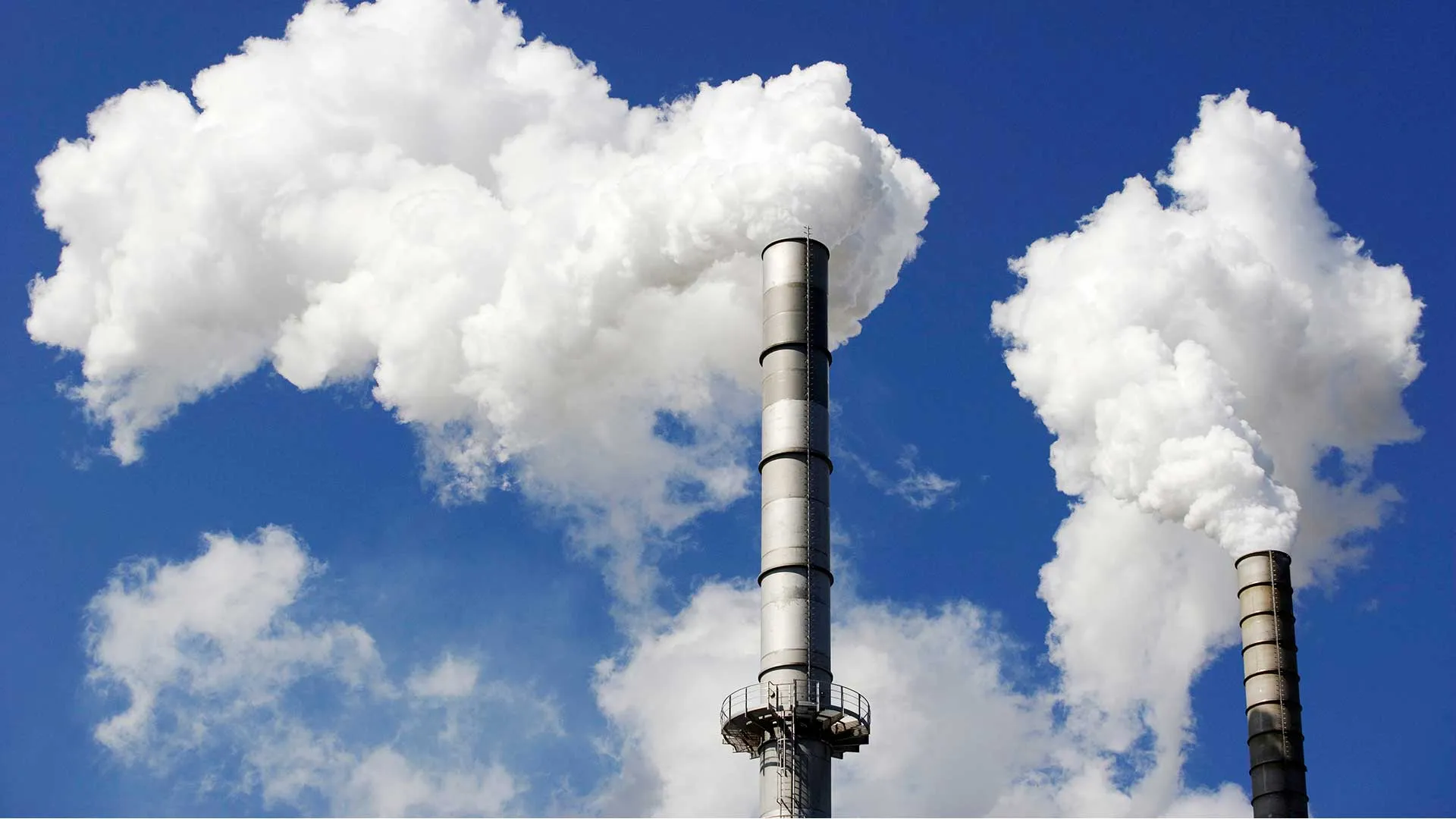 Air emissions billow from two industrial smoke stacks.